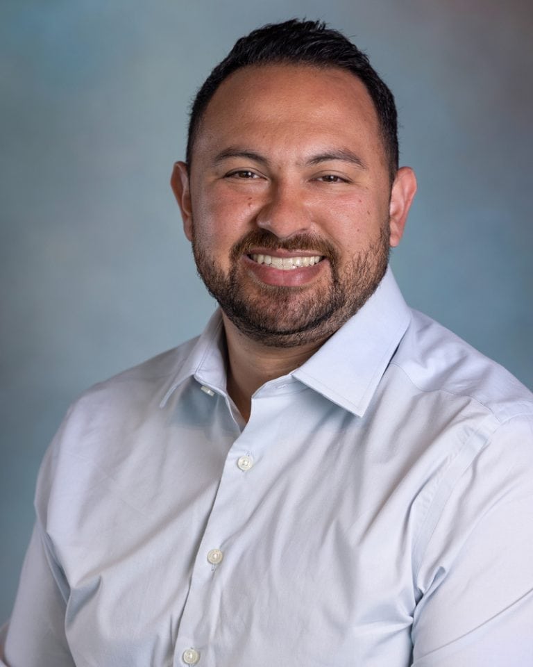 Headshot of Jonathan Herrera smiling, wearing a white shirt, with a neutral background, suitable for business or professional profile.
